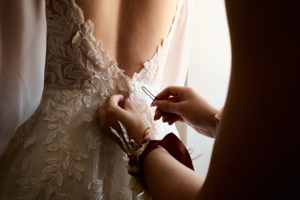 La demoiselle d'honneur boutonne la robe de la mariée.