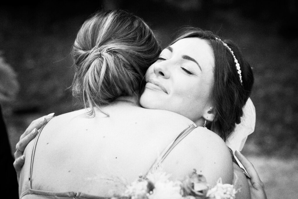 Une larme roule sur la joue de la mariée qui étreint sa demoiselle d'honneur.